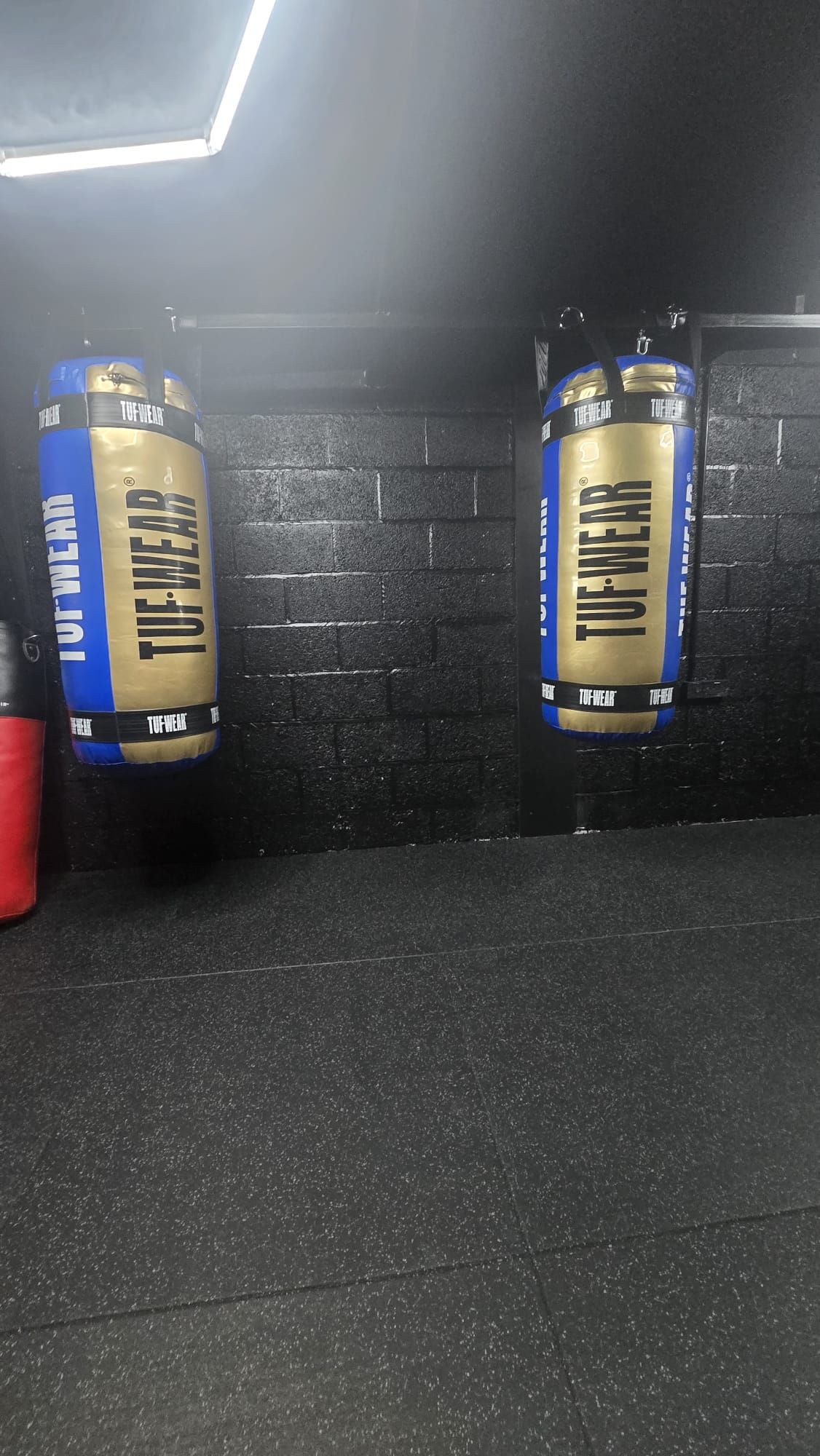 Two blue and gold TUF-WEAR punch bags hanging on a black brick wall